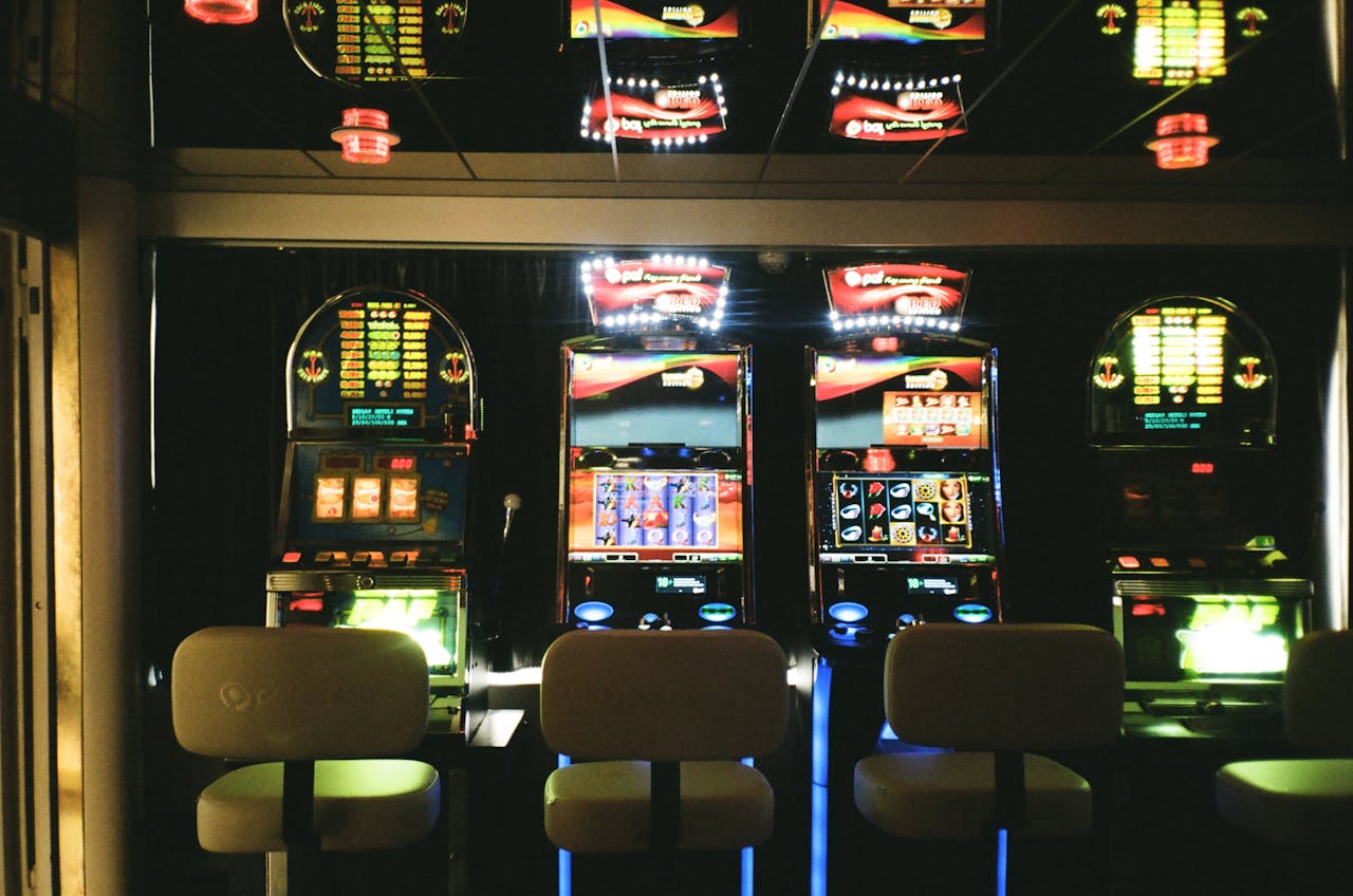about-us Slot machines in a dimly lit casino with reflective ceiling and empty chairs.