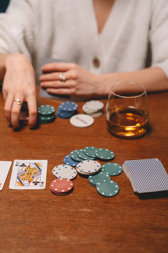 A close-up of a poker game setup on a wooden table with poker chips, cards, and a glass of whiskey.